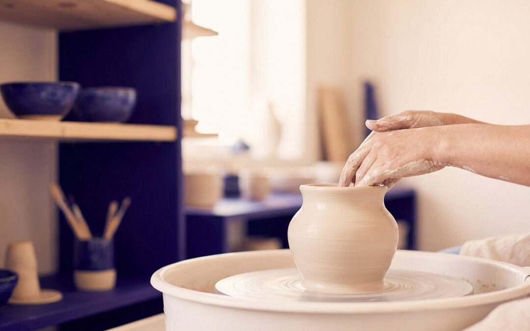 Mains d'un artisan façonnant un vase en argile sur un tour de potier dans un atelier lumineux.