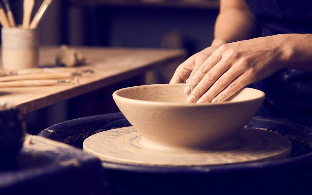 Mains d'un artisan travaillant un bol en argile sur un tour de potier dans un atelier.