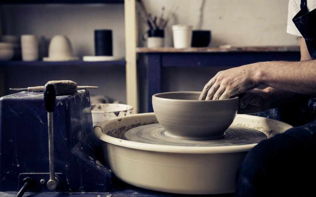 Mains d'un potier façonnant un bol en argile sur un tour de potier dans un atelier.